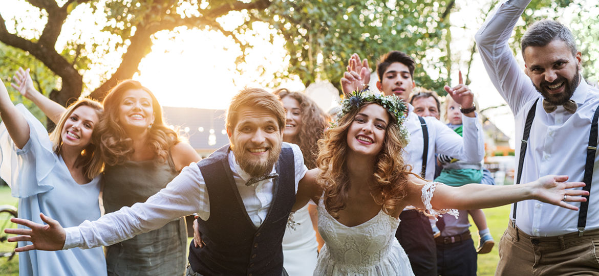 Bride, groom, guests posing for the photo at wedding reception outside in the backyard.