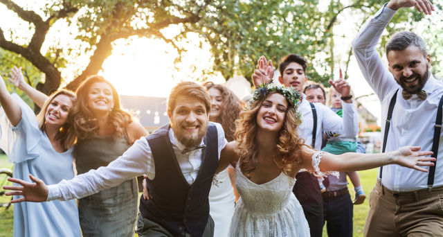 Bride, groom, guests posing for the photo at wedding reception outside in the backyard.