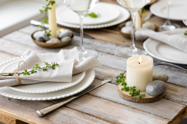 Rustic zero waste wedding decor with natural elements. Wooden table, candles, linen napkins, branches with green leaves. Eco-friendly decoration for the special dinner. Romantic and cozy place