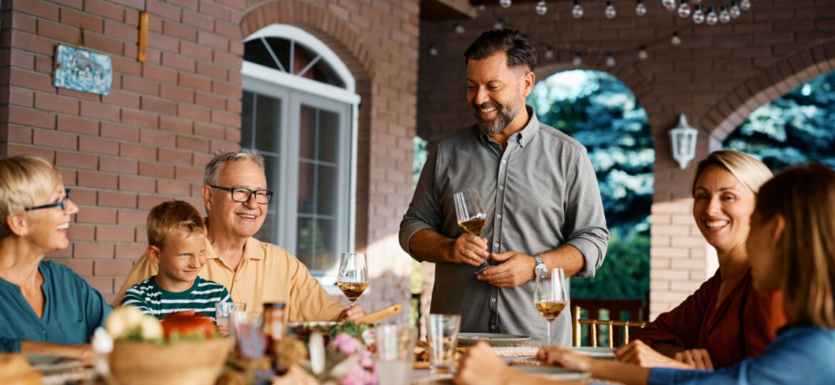 Happy man holding toast during lunch with his extended family on patio.