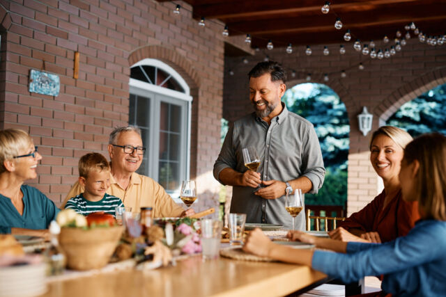 Happy man holding toast during lunch with his extended family on patio.