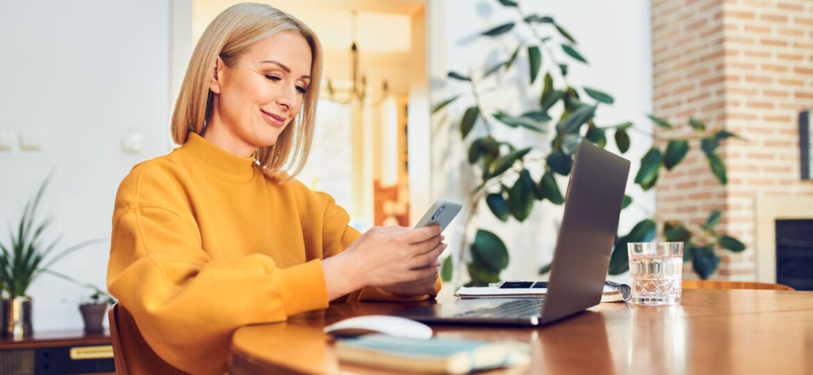 Smiling mid adult woman using smart phone while working remotely at home