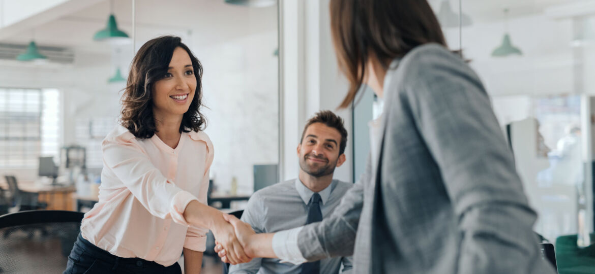 Smiling young businesswoman shaking hands with an office colleague